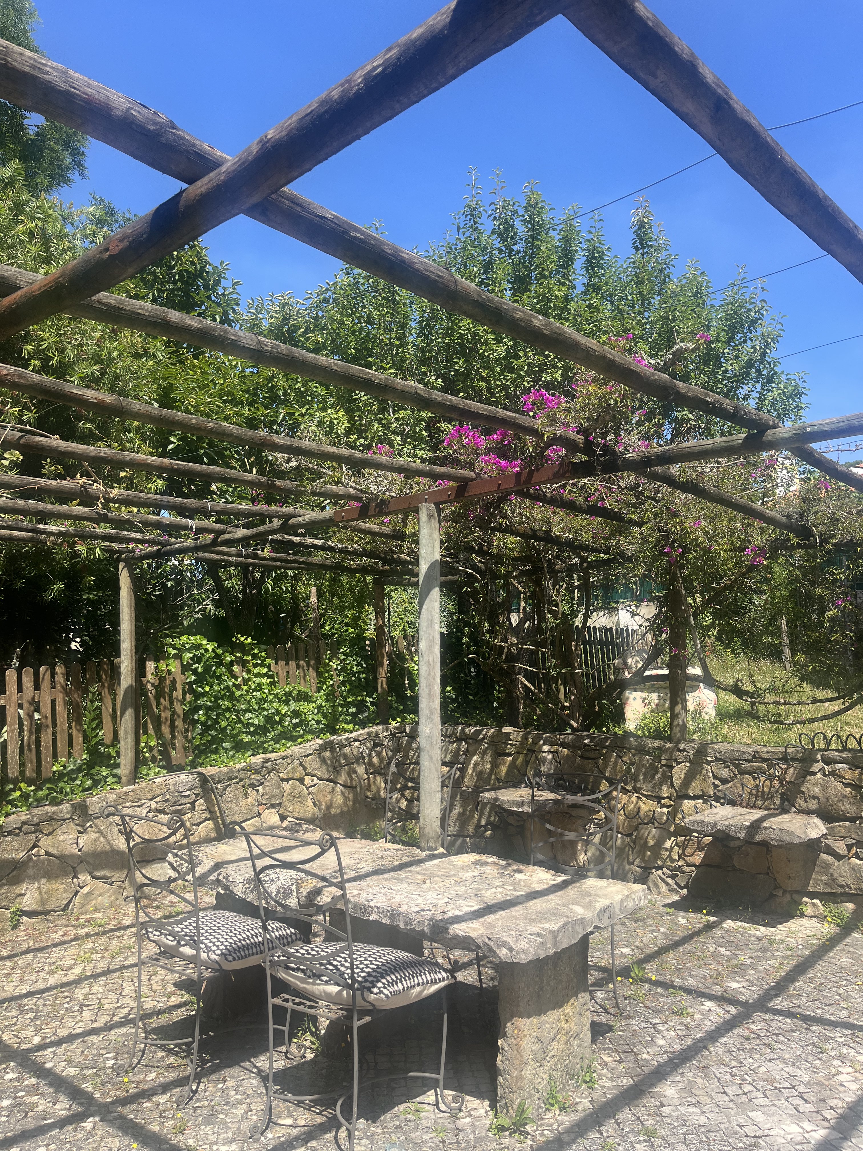 Garden pergola with stone table and chairs under bougainvillea and blue sky